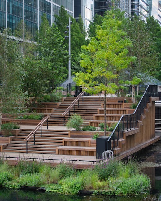 A garden situated beside a canal features a neatly maintained lawn with short, lush grass bordered by a narrow paved pathway. There are various potted plants, including small shrubs and flowering plan